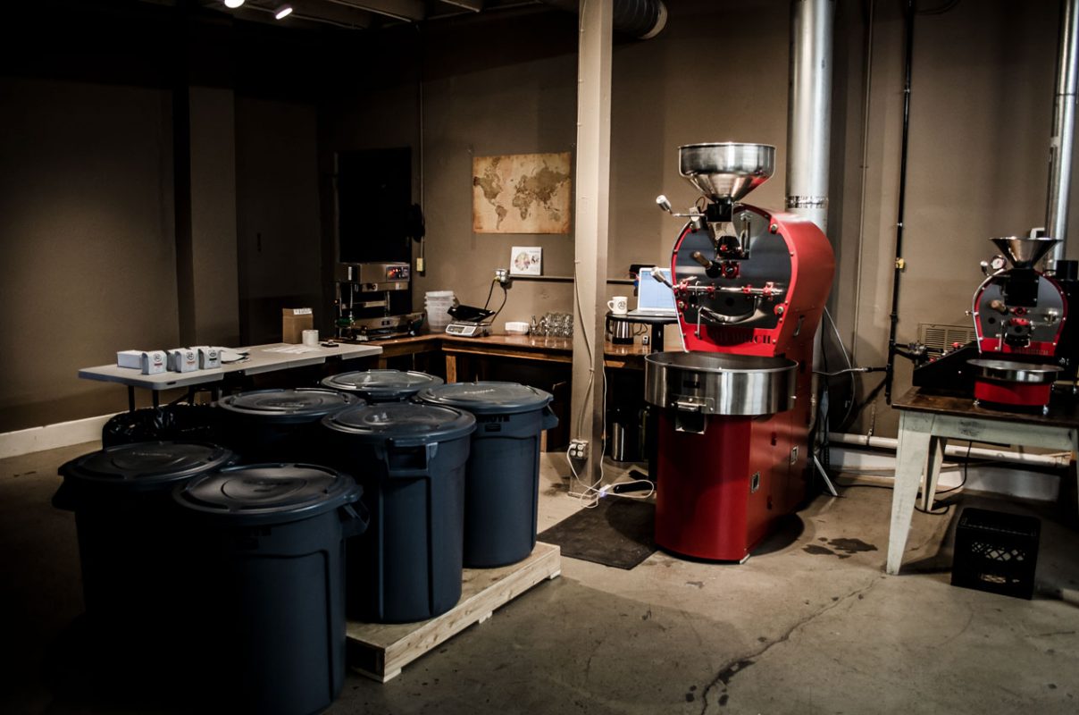 Red coffee bean roaster with bins of unroasted coffee beans - Tin Cup Coffee Company Nashville, TN