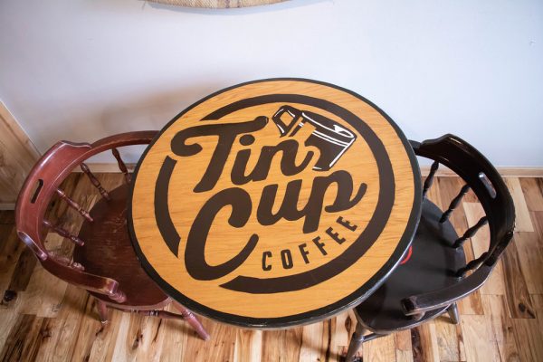 Round, wooden table with a large Tin Cup Coffee Company logo on the table top