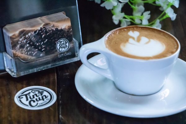 Fresh latte and Tin Cup Coffee Company gift cards on a wooden table